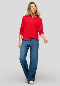 Roter Pullover mit halbhohem Reißverschlusskragen und Fronttasche, kombiniert mit blauen Jeans mit weitem Bein und weißen Turnschuhen. Glatte Textur, lässiges Design.