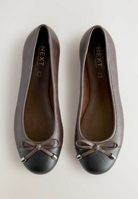 Ballers en cuir marron avec un bout arrondi noir, ornées d'un petit nœud et d'accents métalliques. Texture lisse sur toute la surface.