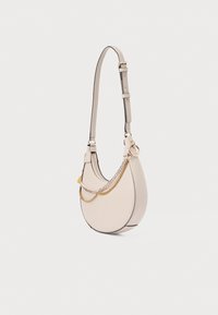 Mała beżowa torebka w kształcie półksiężyca z regulowanym paskiem i dwoma ozdobnymi złotymi i srebrnymi łańcuszkami na jednolitym tle.