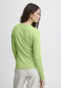 Maglione verde a maniche lunghe in morbido tessuto a maglia, con scollatura rotonda e vestibilità slim, abbinato a pantaloni di colore chiaro.