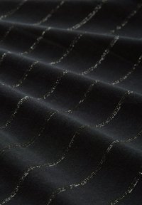 Schwarzer Stoff mit glatter Textur, der wellenförmige silberne Fadenmuster aufweist. Der Glanz des Silbers kontrastiert gegen den dunklen Hintergrund.