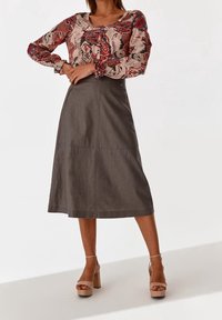 Blouse à manches longues avec un motif floral rouge et crème, associée à une jupe grise mi-longue. Les chaussures présentent des talons épais et compensés.
