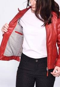 Punainen nahkatakki harmaalla vuorilla, vetskari edessä ja sisätasku. Päällä valkoinen paita, yhdistetty mustiin housuihin, joissa on hillitty kuvio.