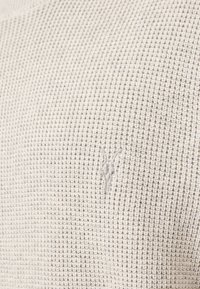 Jasno beżowy sweter o fakturze z wzorem w wafelek. Wyjątkowy detal: małe haftowane logo w nieco ciemniejszym odcieniu beżu.
