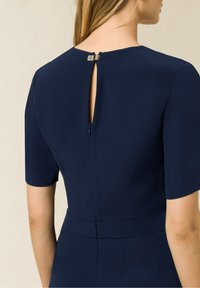 Abito navy con maniche corte, dettaglio a fessura nella parte posteriore e zip discreta. Tessuto liscio con design strutturato e vestibilità sartoriale.