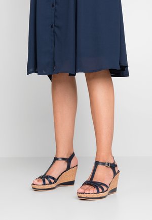 Marineblå kile-sandaler med korkplatform, der har korslagt remme og spænde om anklen. Glat materiale og struktureret midtersål.