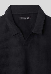 Polo shirt nero con tessuto strutturato, dotato di scollo a v e colletto. L'etichetta riporta "TERRANOVA" e taglia "XL."