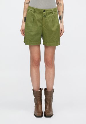 Shorts verts en tissu texturé avec un design plissé, dotés d'une fermeture avant à boutons et de poches latérales. Des bottines marron complètent la tenue.