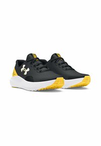 Une paire de baskets de sport noires et jaunes avec des semelles blanches, une texture en mesh, un système de laçage et un logo de marque sur le côté.