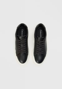 Mustat nahkaiset lenkkarit, joissa on nauhakiinnitys, tekstuuratut mustat yksityiskohdat kantapäässä ja valkoinen kumipohja, jossa on logo sisäpohjassa.