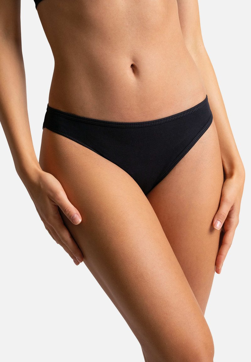 Bas de bikini noir à côtes avec un design taille basse et des bretelles fines sur les côtés. Texture lisse, couverture minimale et aucun élément métallique visible.