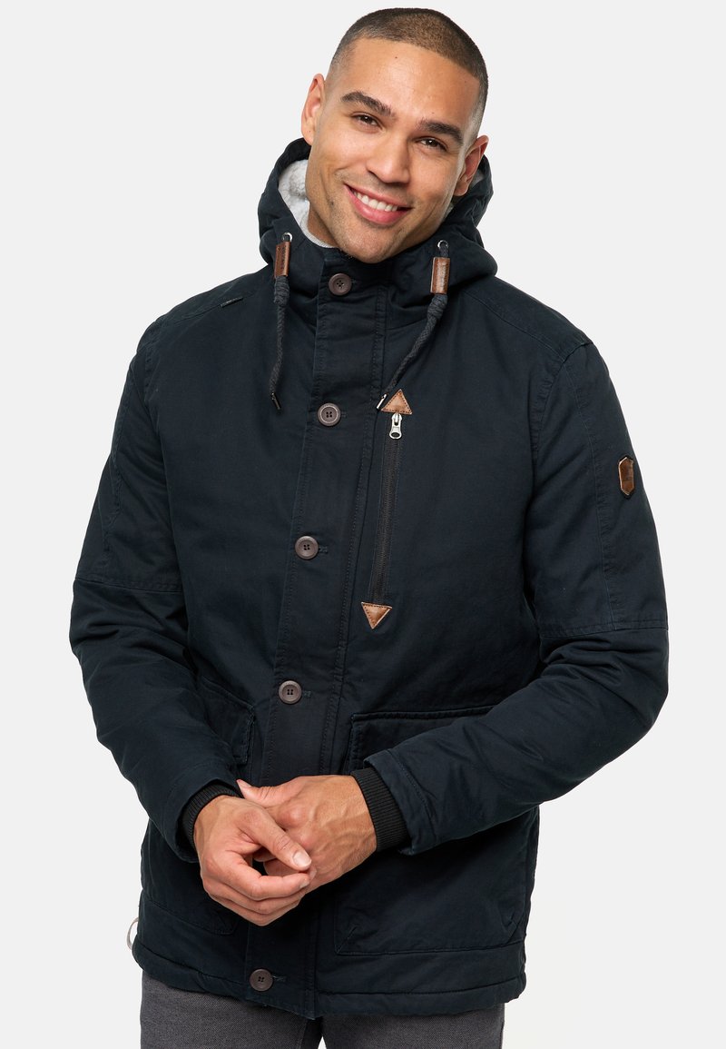 Marineblauwe parka jas met een capuchon met toggles, drukknoopsluiting, een ritsportemonnee op de borst en leren accenten op de kraag.
