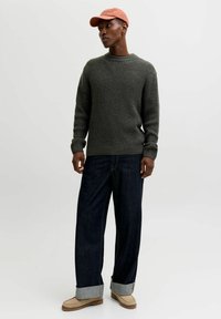 Dark green knit sweater with a ribbed texture, paired with wide-leg dark denim jeans, and beige slip-on shoes. Pink baseball cap completes the look.