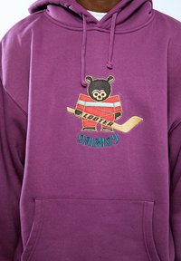 Sudadera morada con un oso como mascota vestido con una camiseta a rayas rojas y azules, sosteniendo un palo de hockey. Texto "LOOTER" y "CRIMESY" bordado.