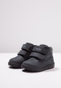 Bottes imperméables bleu foncé avec un extérieur en daim, des sangles Velcro doubles et une semelle en caoutchouc texturée. Logo Geox sur le côté.