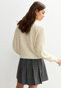Maglione a maglia color crema con vestibilità rilassata e orlo a coste, abbinato a una gonna a pieghe in plaid grigio con linee verticali e orizzontali.