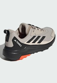 Jasnoszare i czarne buty sportowe z siateczkową cholewką, gumową podeszwą i pomarańczowymi akcentami. Posiadają logo oraz teksturowane detale po bokach.