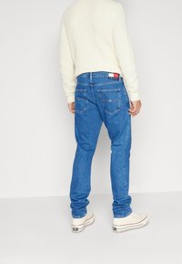 Modré džíny z denimu s klasickým střihem, se dvěma zadními kapsami a páskem s logem značky. Kombinovány s krémovým žebrovaným pleteným svetrem.