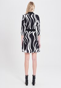 Schwarz-weißes Wellenmuster-Kleid mit Dreiviertelärmeln, tailliertem Schnitt und ausgestellt Rock; kombiniert mit schwarzen Stiefeletten.
