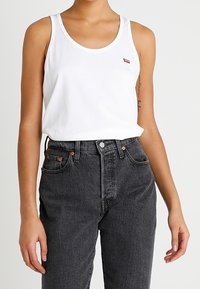 Hvid bomulds tanktop med rund halsudskæring, parret med højtaljede sorte denimjeans med orange hardware og en klassisk pasform.