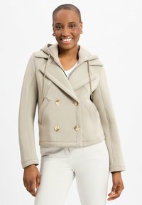 Hellbeige, doppelt geknöpfter Blazer mit Kapuze, ausgestattet mit goldenen Knöpfen und seitlichen Taschen. Glatte Textur und taillierte Passform.