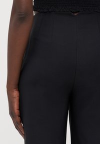 Sorte skreddersydde bukser med glatt stoff, høy midje og side-seam detaljer. Bakslitt med en ren finish og ingen synlig maskinvare.