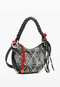 Čierno-biela taška s vzorom, čiernym pleteným úchytom, červenými akcentmi, strieborným kovaním a textúrovaným povrchom. Obsahuje detail prívesku v tvare srdca.