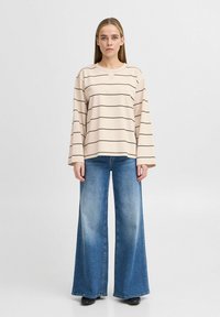 Haut à rayures beige à manches longues avec une coupe décontractée, associé à un jean bleu à coupe large avec un lavage clair et une finition ourlée.