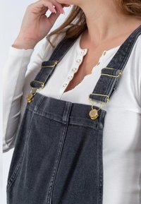 Grijze denim overal met verstelbare gouden hardware, gecombineerd met een witte ribgebreide long-sleeve top met gouden knopen.