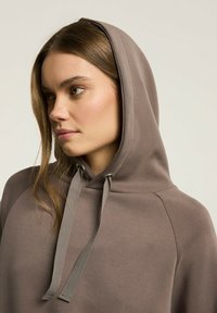 Brązowa bluza z kapturem o gładkiej fakturze. Posiada prosty wzór, kieszeń typu kangur oraz dopasowane sznurki na kapturze.