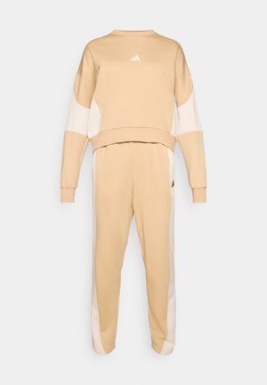 Beige Sweatshirt- und Hosen-Set aus weichem Stoff. Mit kontrastierenden weißen Seitenpaneelen und einem kleinen Logo auf der Brust.
