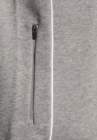 Gray zippered sweatshirt with white piping along the seam. Soft texture and casual design, featuring a detailed zipper pull.