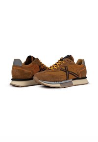 Brown suede and mesh sneakers featuring orange accents, black detailing, and a grey heel cap. Rubber outsole with a textured tread.
