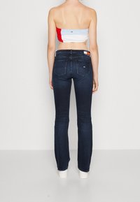 Jeans acampanados de color azul oscuro con una textura desgastada y detalles de costura tradicionales. Cuenta con dos bolsillos traseros y una cintura con marca.