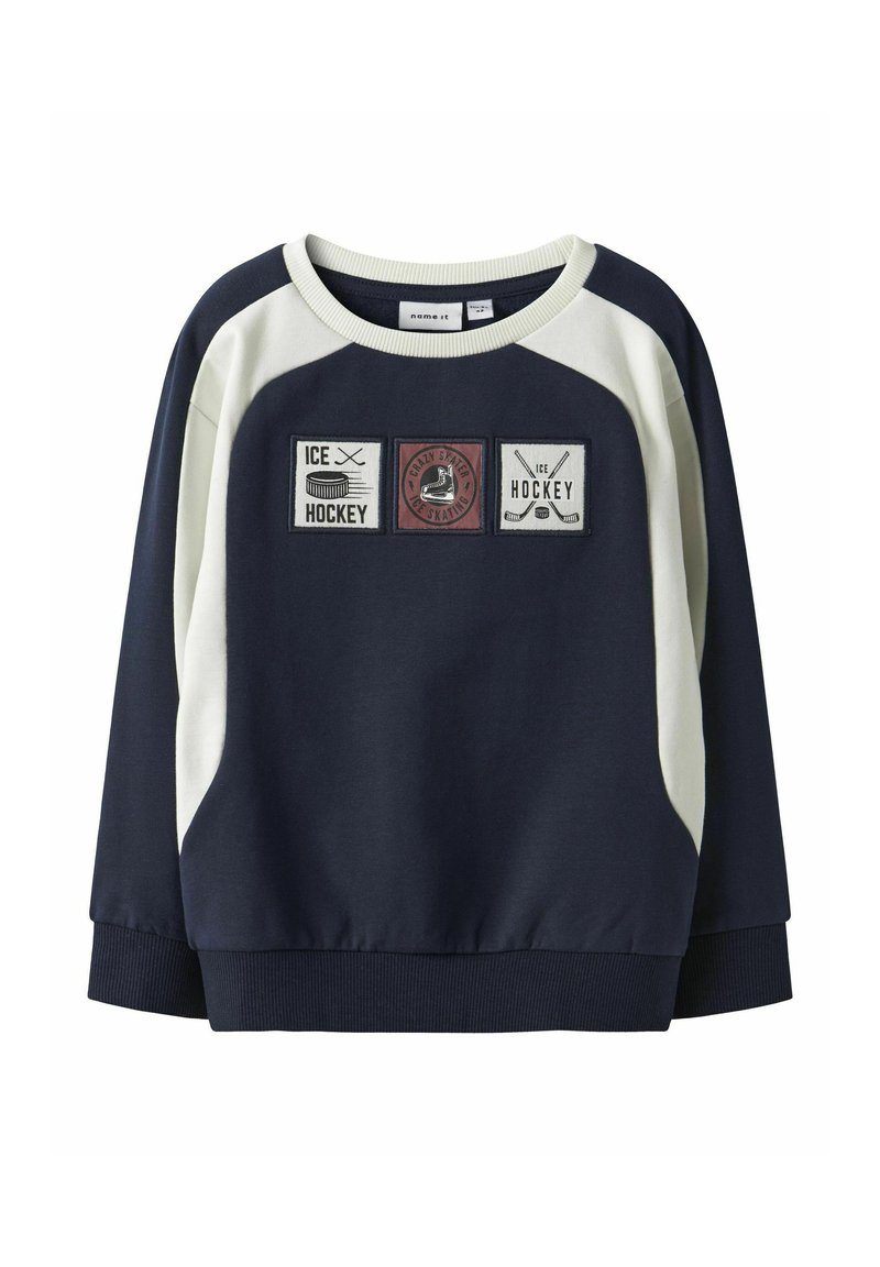 Felpa blu navy con dettagli color crema, caratterizzata da tre toppe ricamate raffiguranti elementi dell'hockey. Collo rotondo e bordo a coste.