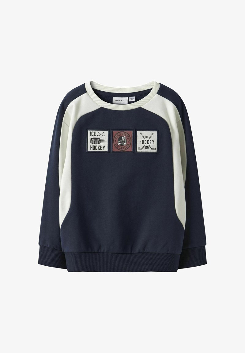 Felpa blu navy con dettagli color crema, caratterizzata da tre toppe ricamate raffiguranti elementi dell'hockey. Collo rotondo e bordo a coste.