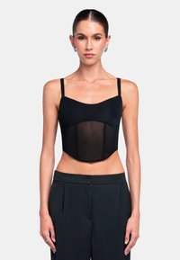 Czarny top bandeau z cienkimi ramiączkami, o dopasowanej sylwetce i przezroczystym panelem na środku. Noszony z czarnymi spodniami o wysokim stanie.