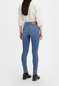 Jeans de tiro alto azul con una textura suave, bolsillos traseros y la característica etiqueta roja de Levi's en la cinturilla. Combinados con una camisa de rayas claras.