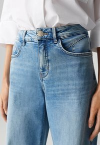 Jean en denim bleu clair avec une coupe droite, dotée d'un bouton en métal, de cinq poches et de détails de décoloration subtils.