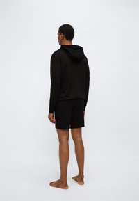 Μαύρο φούτερ με κουκούλα και κορδόνι, συνδυασμένο με μαύρο σορτς. Κατασκευασμένο από απαλό ύφασμα, σχεδιασμένο για κα θημερινή χρήση. Χωρίς ορατά σχέδια ή διακοσμητικά στοιχεία.