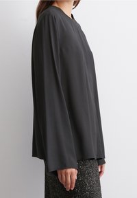 Blusa nera a maniche lunghe con vestibilità morbida, tessuto liscio e scollo rotondo, abbinata a una gonna nera scintillante.