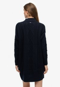 Vestido suéter de punto azul marino con patrones trenzados, cuello alto y mangas largas con puños y bajo acanalados.