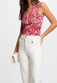 Bodysuit floral rojo con escote en V profundo y detalle anudado en el frente, combinado con pantalones de mezclilla blancos de cintura alta y un bolso de mano blanco.
