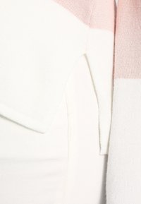 Pull léger en blanc et rose pâle avec une coupe décontractée. Présente une texture tricotée et un ourlet oblique. Convient pour être superposé.