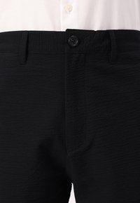 Black textured trousers with a button closure, featuring a smooth fabric, straight cut, and side pockets. Suitable for casual wear.