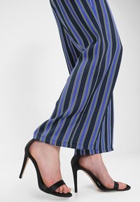 Pantalones de pierna ancha azul marino con rayas verticales blancas y azules, combinados con sandalias de tacón negro con una correa en la parte de los dedos.