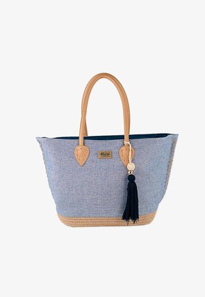 Bolsa tote de tela azul con asas de cuero marrón claro, adorno de borlas y ribete de yute. Cuenta con costuras decorativas en los laterales y un interior espacioso.