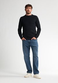Pulover negru texturat cu mâneci lungi, guler rotund și tiv striat, asortat cu blugi drepti de culoare albastră deschisă și teniși albi.