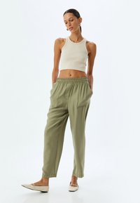 Khaki relax-fit broek met elastische tailleband, zijzakken en een lichtgewicht textuur; gecombineerd met een strakke beige tanktop en platte schoenen.