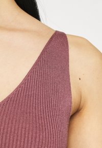 Geribbelde mouwloze top in mauve, met een diepe V-hals en een aansluitende silhouet, die de zachte textuur en gladde naden benadrukt.